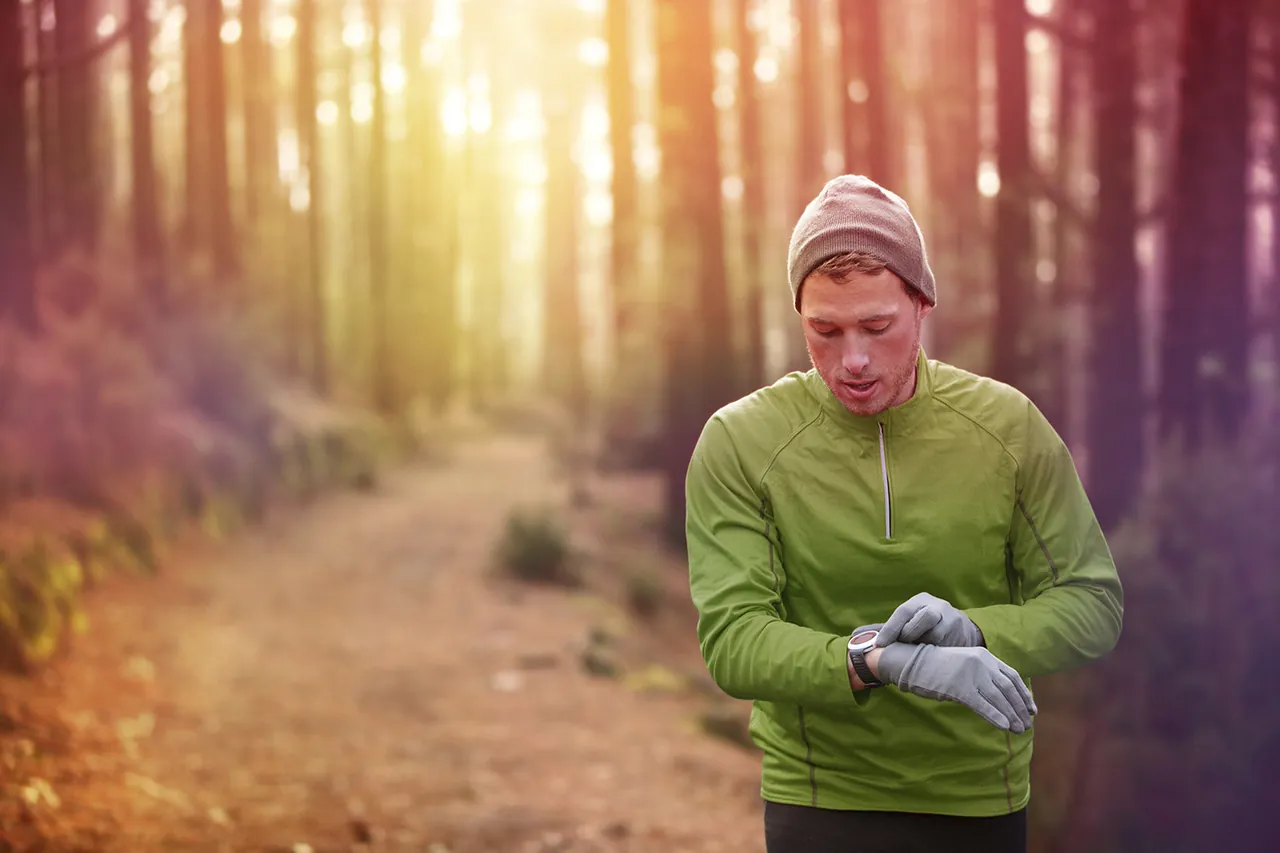 A runner checking the data on his GPS watch on a forest trail