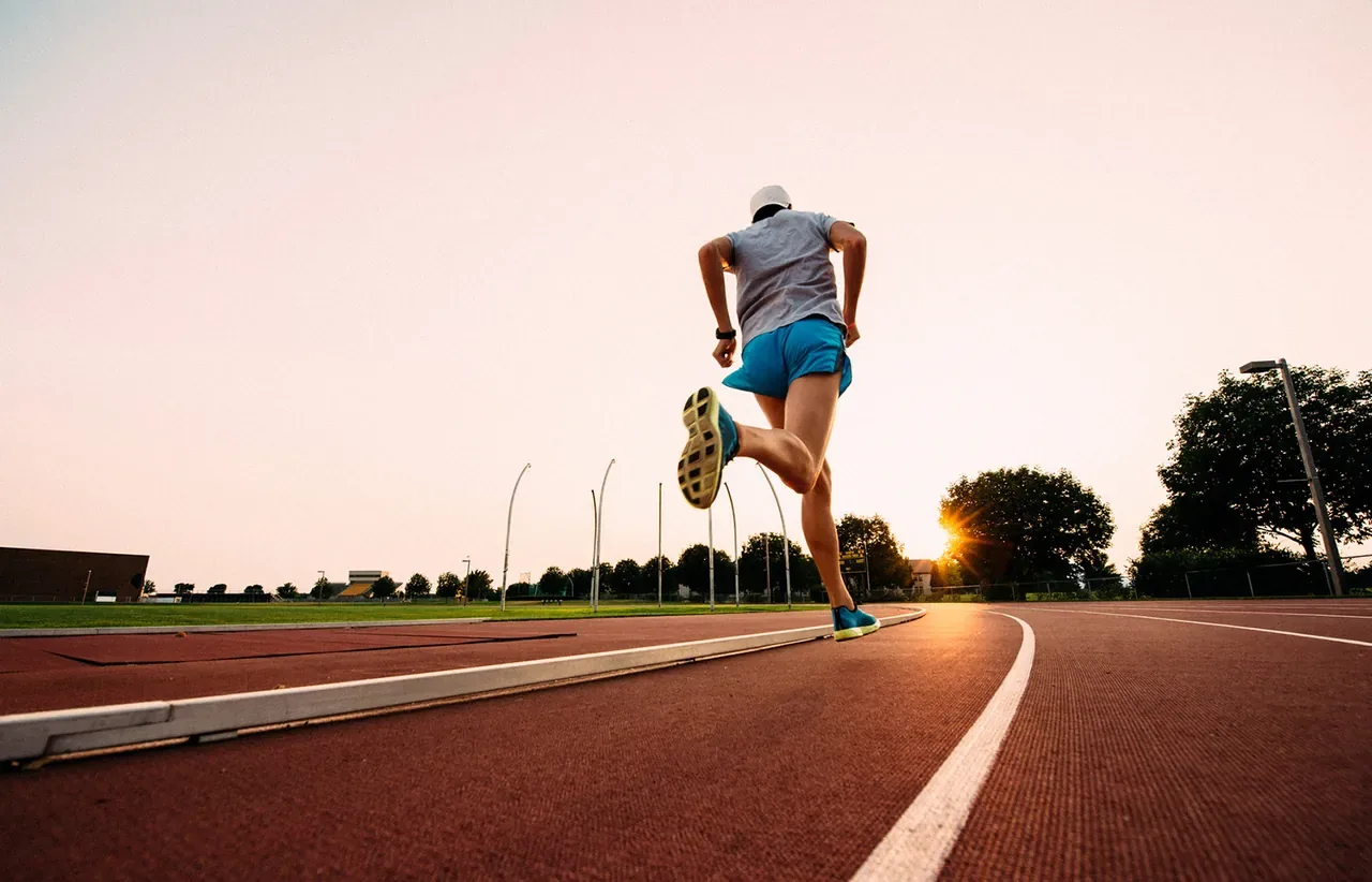 A runner striding around a sunlit track at golden hour
